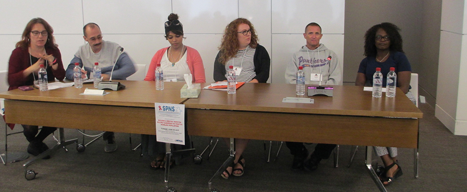 Six people sit at a long table, listening intently.