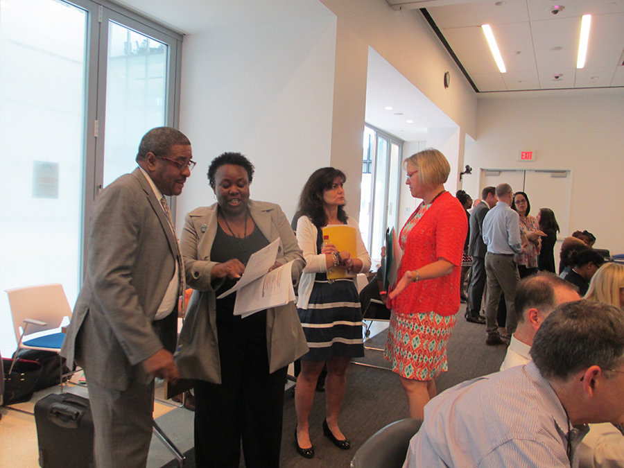 Four people talking together seriously, looking at document, at the back of the meeting room.