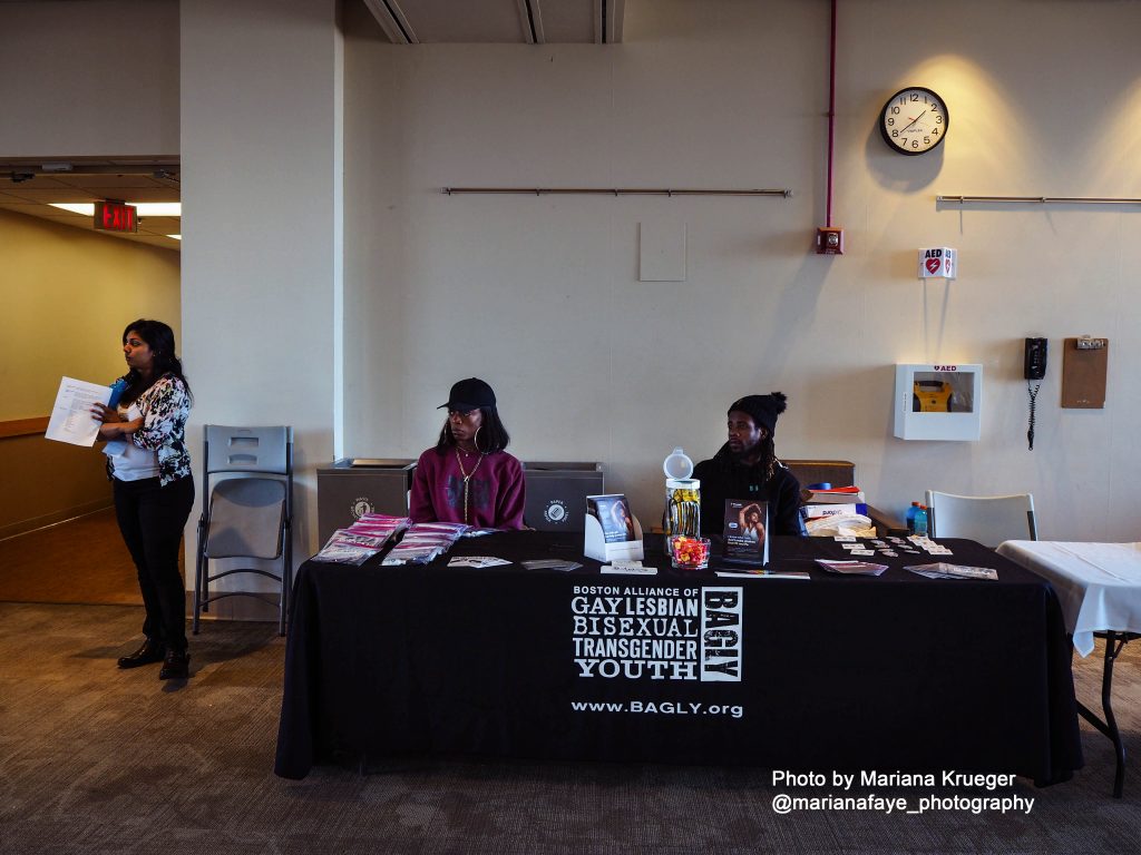 Two people seated behind a table with a banner displaying the BAGLY logo and URL (www.BAGLY.org)