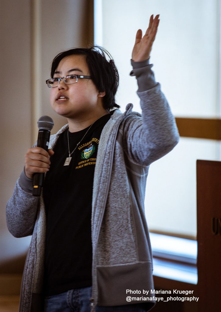 Lydia Brown speaking into a hand-held microphone while raising the other hand.